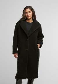 Cappotto lungo nero, texturizzato, in morbido tessuto con colletto a ribadire, chiusura frontale con bottoni e tasche laterali, caratterizzato da una vestibilità rilassata.