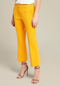 Geel op maat gemaakte broek met een aansluitende taille, rechte pijpen en zijzakken. Gepaard met bruine enkellaarsjes met een bandje.