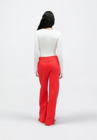 Λευκό μπλουζάκι μακρυμάνικο με κόκκινες ραφές, σε συνδυασμό με κόκκινο παντελόνι φαρδιάς γραμμής που φέρει λογότυπο "NIKE SHOX" στη πίσω ζώνη μέσης.