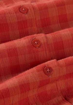 Tissu à carreaux rouge-orangés doux avec trois boutons marron assortis cousus en rangée verticale.