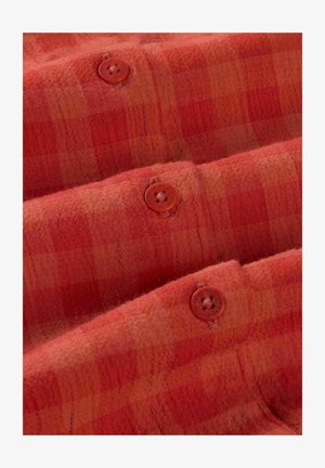 Tissu à carreaux rouge-orangés doux avec trois boutons marron assortis cousus en rangée verticale.