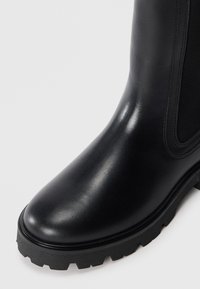 Black leather ankle boot with a smooth finish, round toe, elastic side panel, and rugged rubber sole. Minimalist design, no visible logos.