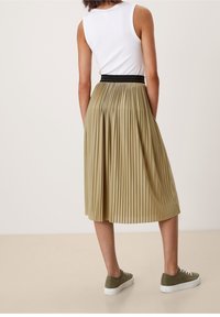 Gonna khaki plissettata con vita nera, abbinata a sneakers verdi, vista da dietro. Il tessuto ha una texture liscia e un design fluido.