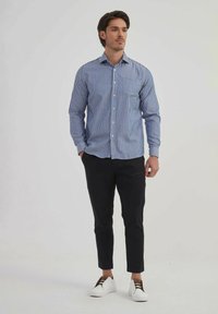 Chemise à boutons bleu rayée avec une poche poitrine, associée à un pantalon noir slim et des baskets blanches avec des accents marron.