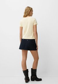 Korte mouwen gele t-shirt in combinatie met een donkere denim minirok. Zwarte kniehoge laarzen met gespaccenten. Glad materiaal en eenvoudig ontwerp.
