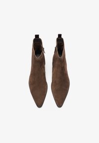 Botas de ante marrón hasta el tobillo con punta afilada, que cuentan con cremalleras laterales y un tirador en la parte trasera. Textura suave y diseño minimalista.