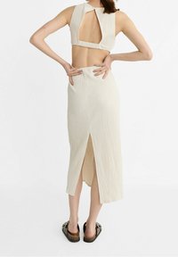 Ensemble deux pièces de couleur crème avec une finition texturée. Le haut présente un dos en œillet, et la jupe a une fente à l'avant.