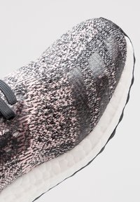 Kraťas na atletickou obuv v černé a růžové barvě s třemi tmavými translucentními pruhy na bílé texturované podrážce, pohled z přední šikmé strany.