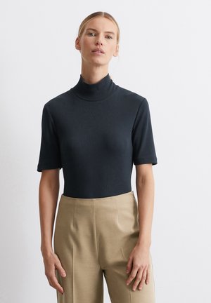 Schwarzer gerippter Rollkragenpullover mit kurzen Ärmeln, figurschmeichelndes Design, kombiniert mit beigen, hochtaillierten Hosen, glatte Textur.