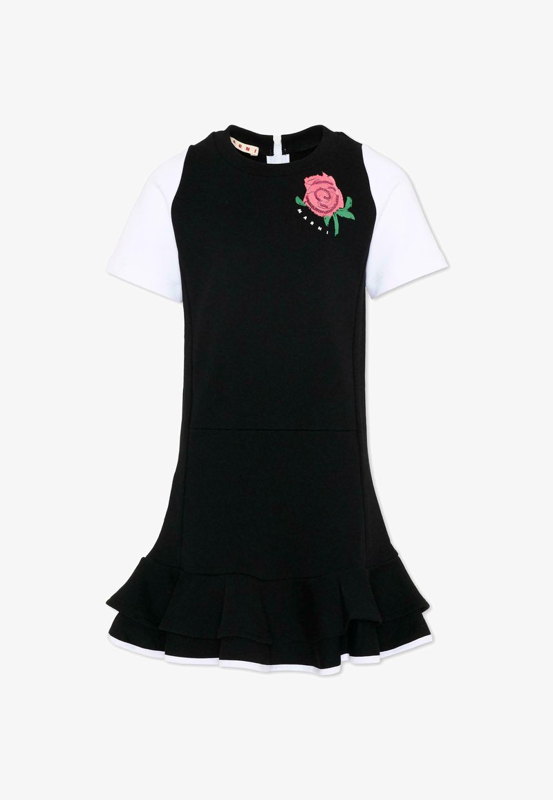 Robe noire sans manches superposée à une chemise blanche à manches courtes, broderie de rose rose près de l'épaule et détail de ourlet à volants.