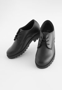 Chaussures en cuir noir avec un bout arrondi, un laçage sur le devant et une semelle en caoutchouc texturée avec des crampons bien marqués pour une meilleure adhérence.