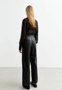 Svart genomskinlig långärmad topp kombinerad med högmidjade svarta faux läderbyxor. Har rak skärning, minimalistisk design och bakfickor.