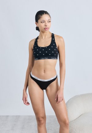 Μαύρο αθλητικό μπουστάκι με μοτίβο λογότυπου και φα ρδιά ζώνη· συνδυασμένο με μαύρο στρινγκ με λευκή ζώνη μέσης με λογότυπο· απαλό ύφασμα, εφαρμοστό σχέδιο.