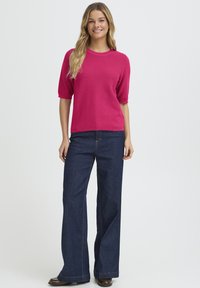 Fuksija kratka pamučna majica s okruglim izrezom, uparena s visokim strukom tamnoplavih širokih traperica s vidljivim šavovima i džepovima.