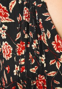 Top in tessuto nero con motivi floreali rossi e crema, design plissettato e sottili dettagli lucidi lungo le cuciture.