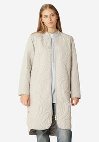 Abrigo acolchado gris claro con patrones texturizados en espiral, mangas largas, frente abierto y corte recto, llevado sobre una blusa azul clara y jeans.