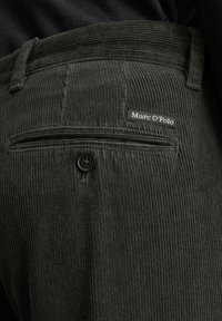 Tmavě zelené manšestrové kalhoty s vertikálním proužkováním, vybavené zadní kapsou s knoflíkem a štítkem značky "Marc O'Polo."