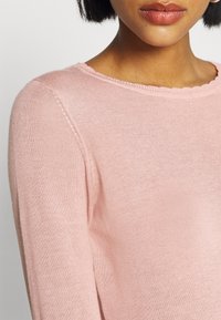 Rosa tröja i fint stickat material, med en klassisk rund halsringning och subtila ribbade detaljer längs kragen.