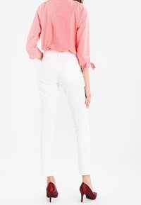 White fitted pants paired with a red and white striped blouse featuring three-quarter sleeves and tie details. Model wears burgundy heels.