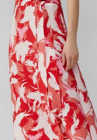 Robe maxi à motifs rouges et roses avec une taille nouée, présentant des designs de coups de pinceau ondulés et un tissu texturé.