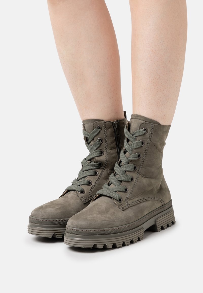 Stivaletti alla caviglia in suede verde con lacci frontali, zip laterale e suole robuste. Presentano un motivo testurizzato e dettagli di cucitura.