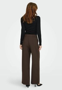 Weite braune Hosen mit glatter Textur, ausgestattet mit tailliertem Bund und Taschen, ergänzt durch schwarze High Heels.
