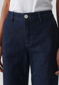 Donkerblauwe denimbroek met een rechte snit, voorzien van een metalen knoop in de taille en subtiele stikdetails door de stof heen.