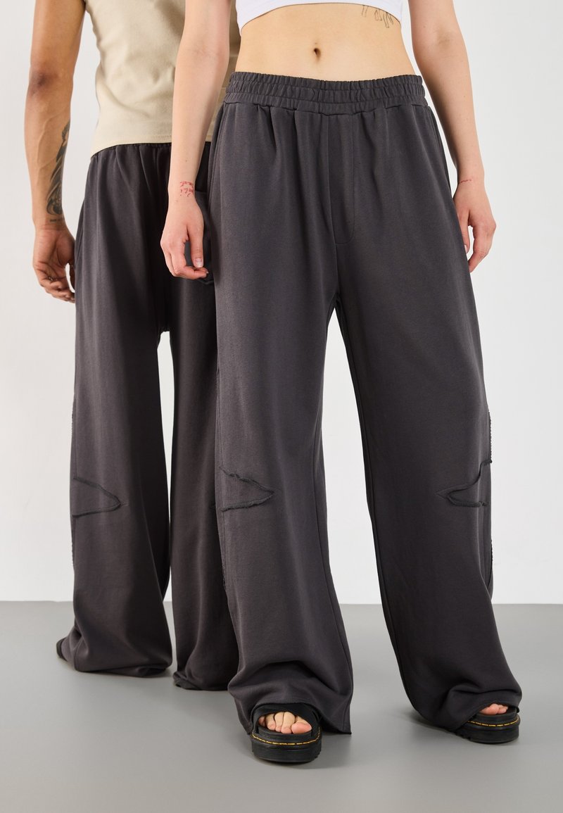 Dark gray wide-leg pants featuring a soft fabric, elastic waistband, and distinct knee cutouts with frayed edges. Paired with platform sandals.