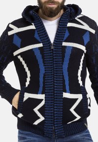 Marineblauer Reißverschluss-Hoodie mit geometrischen blau-weißen Mustern, gestrickter Textur, zwei vorderen Taschen und einer gerippten Bündchen- und Saumkante.