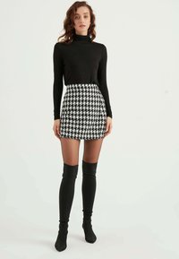 Maglione aderente nero a collo alto abbinato a una mini gonna a scacchi. Stivali neri alti fino alla coscia completano l'outfit.