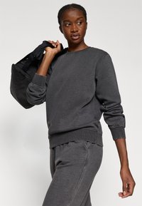 Hallitusest hallid dressiped ja sobivad püksid, mis on valmistatud pehmest kangast. Dressipluusil on mansetid ja soonikserv. Mudel hoiab käes musta kotti.