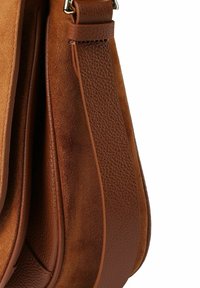 Braune Lederhandtasche mit glatter Textur, kontrastierendem Wildledereinsatz und geschwungenem Design mit elegantem Riemen.