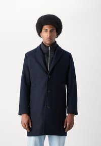 Abrigo de mezcla de lana en color navy con cuello muesca, botones frontales y diseño de dos capas que cuenta con una capa interna acolchada negra. Tejido texturizado.