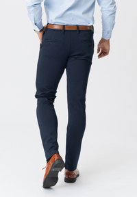 Mørkeblå bukser med slim fit, der har baglommer og en glat tekstur, parret med brune lædersko.