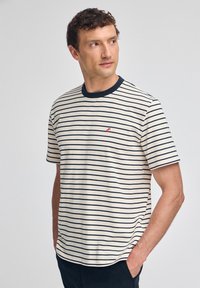 Koszulka z bawełny w paski z okrągłym dekoltem, krótkimi rękawami i czerwonym haftowanym logo po lewej stronie klatki piersiowej. Kolory: kremowy i granatowy.