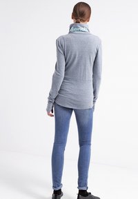 Maglione grigio a maniche lunghe con colletto alto, decorato con il logo blu "Bench", abbinato a jeans blu e scarpe nere. Tessuto a trama, vestibilità slim.
