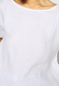 Valkoinen pellavapaita, jossa on rento istuvuus, pyöreä pääntie ja lyhyet hihat. Kankaassa on luonnollinen rakenne ja hieno läpikuultavuus.