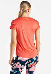 Camiseta atlética de manga corta en color coral con un corte relajado. Presenta un escote redondo y una textura suave, combinada con leggings estampados.