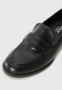 Black leather loafer with a smooth finish, featuring a stitched moc toe and a front strap accent. Slim profile with a low heel.