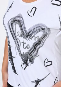 Camiseta blanca con diseño de corazón en negro y plata, con el texto "Llévame a París" e ilustraciones de la Torre Eiffel, tela suave.