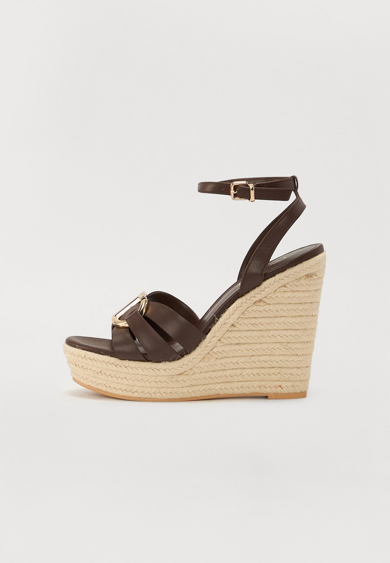 Brown wedge sandal with a woven jute sole, leather straps, and a gold buckle accent. Ankle strap design with a wide toe band.