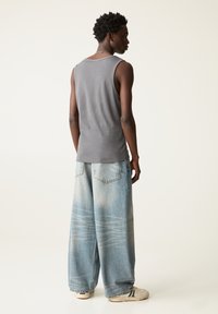 Débardeur gris à coupe décontractée, associé à un jean en denim large bleu clair avec un délavage et des motifs subtils.
