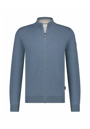 Nahaufnahme des unteren Gesichts und Halses eines Mannes, der einen blauen, gerippten Pullover mit teilweise geschlossenem Reißverschluss trägt.