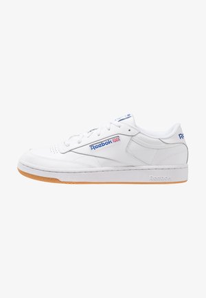 Witte sneakers met een glad leren bovenkant, in contrast met een rubberen gumzool. Heeft blauwe branding en een vetersluiting.