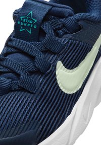 Zapatilla atlética azul marino con un upper texturizado, un swoosh de Nike en verde claro y un logo en forma de estrella en la lengua. Suela de goma y cierre de cordones.