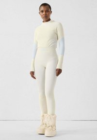 Conjunto térmico crema claro con mangas largas y cuello alto. Complementado con leggings ceñidos y texturizados y botas blancas acolchadas.