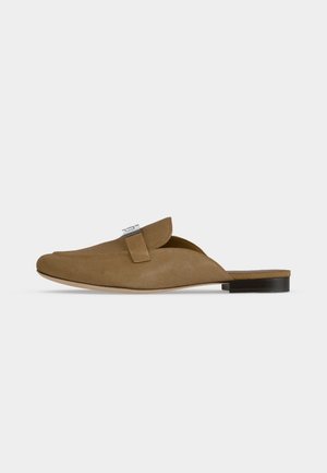 Mule en daim marron à enfiler avec un bout pointu, détail boucle argentée, et talon plat noir sur fond blanc.