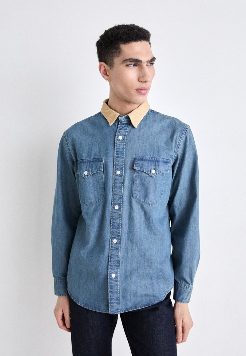 Denim shirt in light blue with a contrasting beige collar, long sleeves, two chest pockets, and button front closure. Soft texture.