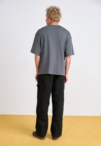T-shirt en coton gris à manches courtes et coupe décontractée, associé à un pantalon cargo noir. Texture lisse ; design simple et neutre.