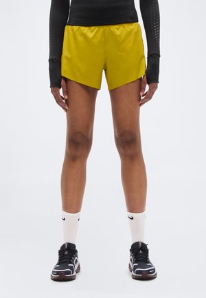 Gule løbeshorts med et chevrondesign, kombineret med en sort langærmet top. Båret med sorte sneakers og hvide sokker med et logo.